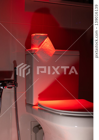 Roll of toilet paper on a white cistern in a dark red light. Conceptual visualization of bowel movement problem, digestive health issue, or gastrointestinal symptom. photography Roll of toilet paper on a white cistern in a dark red light. Conceptual visualization of bowel movement problem, digestive health issue, or gastrointestinal symptom. photography 139016139