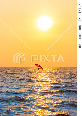 A lone windsurfer glides across the ocean under a glowing golden sunset. A lone windsurfer glides across the ocean under a glowing golden sunset. 139016197
