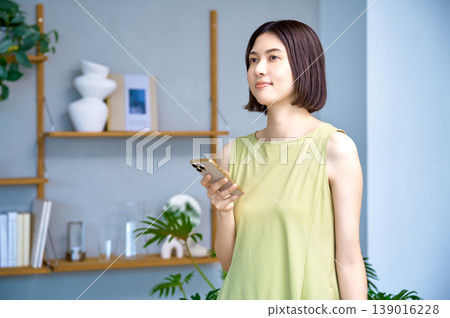 一位年輕女性在現代客廳使用智慧型手機的生活方式。 一位年輕女性在現代客廳使用智慧型手機的生活方式。 139016228