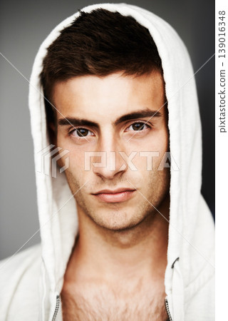 Serious, portrait and man in hoodie for fashion isolated on a gray background. Confident young person, face of model and streetwear clothes, casual and cool facial expression in Spain on a backdrop Serious, portrait and man in hoodie for fashion isolated on a gray background. Confident young person, face of model and streetwear clothes, casual and cool facial expression in Spain on a backdrop 139016348