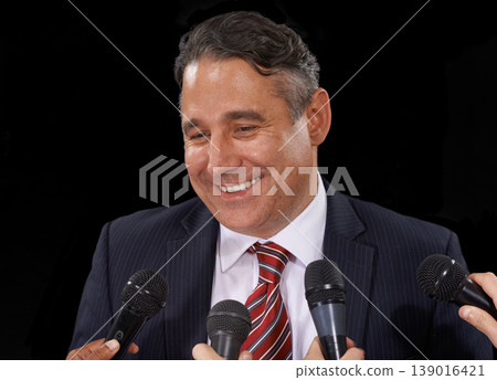 Man, speech and politician at press conference to media for election, forum or broadcast to audience in studio on black background. Politics, government and happy public speaker talking at microphone Man, speech and politician at press conference to media for election, forum or broadcast to audience in studio on black background. Politics, government and happy public speaker talking at microphone 139016421