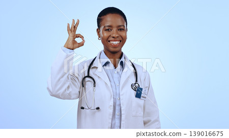 Portrait, okay or happy black woman doctor with smile or confidence isolated on blue background. Wellness, studio or female African healthcare worker with approval sign, success or yes hand gesture Portrait, okay or happy black woman doctor with smile or confidence isolated on blue background. Wellness, studio or female African healthcare worker with approval sign, success or yes hand gesture 139016675