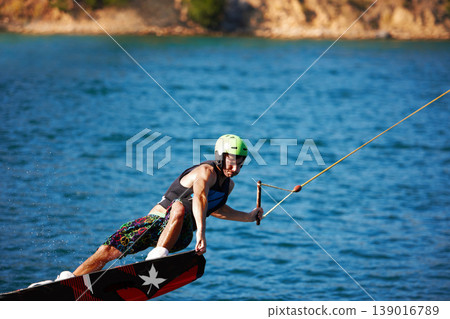 Man, wakeboarding outdoor and lake with helmet, sport and fitness for speed in summer sunshine. Person, athlete and ski with rope for safety on water, sea or river for training, exercise and freedom 139016789