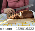 person cuts black bread on wooden board with knife. Sourdough rye bread with crispy crust. 139016822