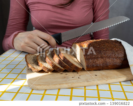 person cuts black bread on wooden board with knife. Sourdough rye bread with crispy crust. person cuts black bread on wooden board with knife. Sourdough rye bread with crispy crust. 139016822