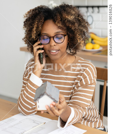 female architect or realtor holds mock up of house in her hands, talks on phone with client. 139016826