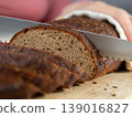 person cuts black bread on wooden board with knife. Sourdough rye bread with crispy crust. 139016827
