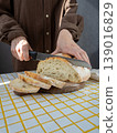 person cuts white bread on wooden board with knife. homemade sourdough bread with crispy crust. 139016829
