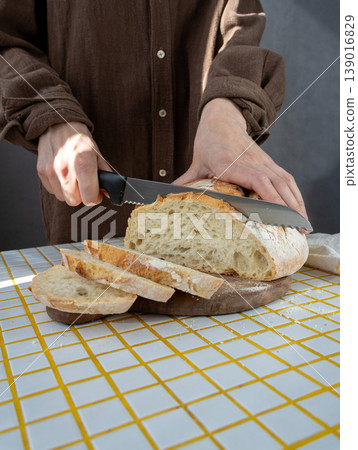 person cuts white bread on wooden board with knife. homemade sourdough bread with crispy crust. person cuts white bread on wooden board with knife. homemade sourdough bread with crispy crust. 139016829