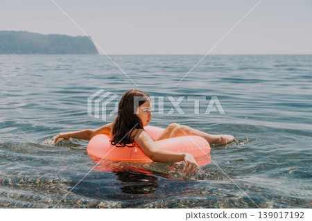 Girl swimming sea relaxing in pink inflatable ring on calm ocean water with coastal mountains background 139017192