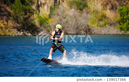 Man, wakeboarding and water with helmet, sport and fitness for speed on vacation in summer sunshine. Person, athlete and ski with rope for safety on lake, sea or river for training, exercise or waves Man, wakeboarding and water with helmet, sport and fitness for speed on vacation in summer sunshine. Person, athlete and ski with rope for safety on lake, sea or river for training, exercise or waves 139017366