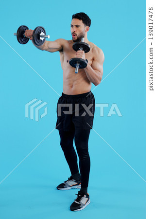 Dumbbells, fitness and man in studio for training, exercise or bodybuilding on blue background. Health, wellness and topless guy bodybuilder with bicep workout, muscle or flex, progress or resilience 139017478