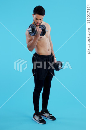 Fitness, dumbbells and man flex in studio for training, exercise or bodybuilding on blue background. Health, wellness or topless bodybuilder with bicep workout, muscle or body, progress or resilience 139017564