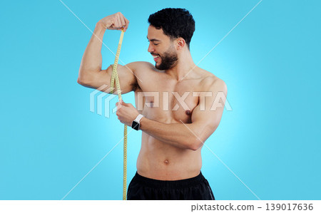 Happy man, measuring tape and bicep in fitness, bodybuilding or weight loss against a blue background. Male person, athlete or bodybuilder smile taking muscle or arm measurement for flex on mockup 139017636