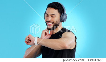Happy man, headphones and checking watch for pulse in fitness against a blue studio background. Male person, athlete or model looking at wristwatch for monitoring performance or heart rate on mockup 139017643