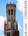 Sunny view of the Belfry of Bruges rising above the historic Markt square, showcasing medieval Flemish architecture under a clear blue sky, Brugge, West Flanders, Belgium 139018248