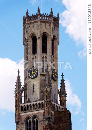 Sunny view of the Belfry of Bruges rising above the historic Markt square, showcasing medieval Flemish architecture under a clear blue sky, Brugge, West Flanders, Belgium 139018248