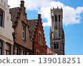 Sunny view of the Belfry of Bruges rising above the historic Markt square, showcasing medieval Flemish architecture under a clear blue sky, Brugge, West Flanders, Belgium 139018251