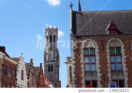 Sunny view of the Belfry of Bruges rising above the historic Markt square, showcasing medieval Flemish architecture under a clear blue sky, Brugge, West Flanders, Belgium 139018253