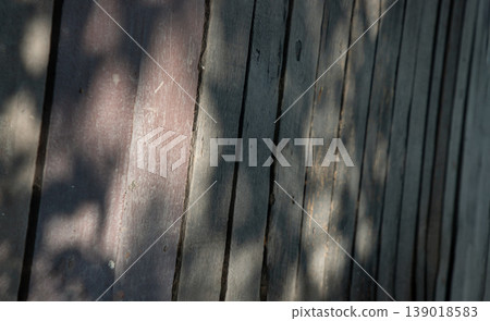 A series of weathered, vertically oriented wooden planks forms a textured surface, highlighted by bright, irregular patches of sunlight. Deep gaps and visible scratches give the wood a rustic, aged. A series of weathered, vertically oriented wooden planks forms a textured surface, highlighted by bright, irregular patches of sunlight. Deep gaps and visible scratches give the wood a rustic, aged. 139018583