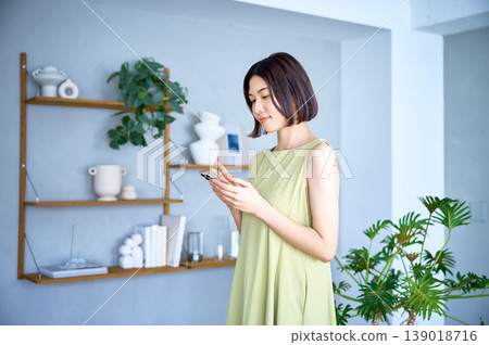 A relaxed young Japanese woman using her smartphone in her room. A relaxed young Japanese woman using her smartphone in her room. 139018716