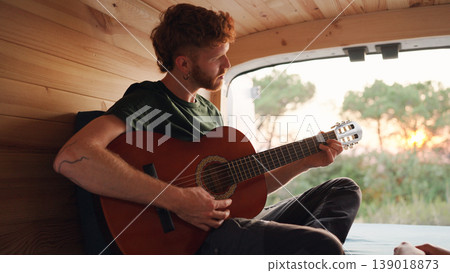 Man playing guitar inside camper van at sunset Man playing guitar inside camper van at sunset 139018873