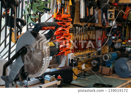 Workshop tools wall. Carpentry equipment. Collection of professional joiner accessories with electric miter saw placed on workbench. Workshop tools wall. Carpentry equipment. Collection of professional joiner accessories with electric miter saw placed on workbench. 139019172