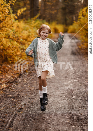 Leafstrewn Walk With Joyful Girl. Happy Girl In Cozy Attire Strolling Through Autumn Landscape 139019243