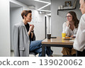 Businesswomen discussing work at kitchen table with drinks and snacks in modern office. Discussion, kitchen, drinks, snacks, teamwork, businesswomen. 139020062