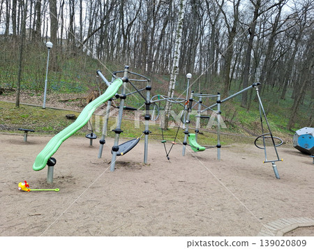 Kids can enjoy climbing on structures and using a green slide in a playground surrounded by trees. The area is designed for outdoor fun and activities for children. 139020809