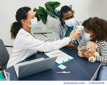 General practitioner checking body temperature of a child patient using infrared thermometer. African American girl with her daddy wearing protective masks at the doctor's consultation 139020848