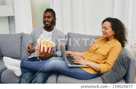 Family life of couple. Husband watching TV near to wife who surfs internet on his laptop sitting on couch 139020877