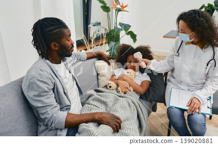 House call doctors. Pediatrician measures temperature of a little girl patient with cold and flu using infrared thermometer at home. Medical help at home House call doctors. Pediatrician measures temperature of a little girl patient with cold and flu using infrared thermometer at home. Medical help at home 139020881