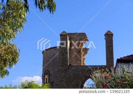 A historic stone tower rises against a clear blue sky surrounded by vibrant greenery in a peaceful setting 139021185
