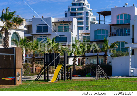 Colorful playground under palm trees beside modern beachside apartments in sunny weather Colorful playground under palm trees beside modern beachside apartments in sunny weather 139021194