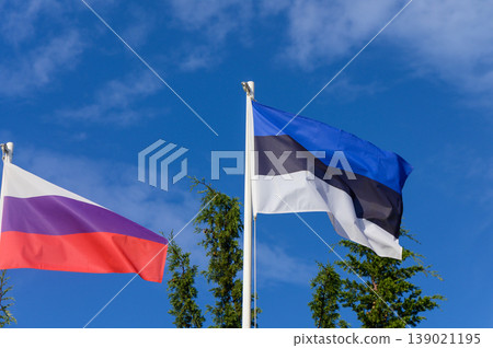 Flags of Estonia and Russia wave in the gentle breeze against a bright blue sky during a sunny day Flags of Estonia and Russia wave in the gentle breeze against a bright blue sky during a sunny day 139021195