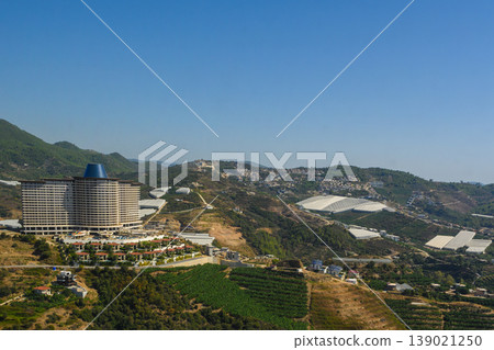 Scenic view of a modern hotel nestled in lush green hills under a clear blue sky 139021250