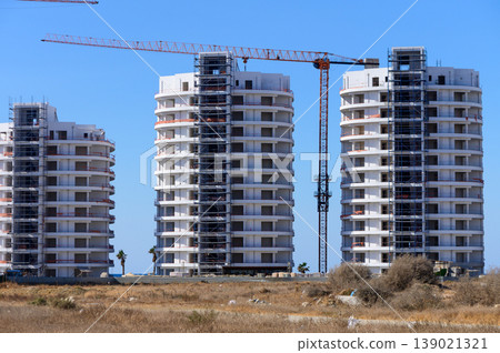 New residential buildings under construction with cranes in a sunny location near the coastline New residential buildings under construction with cranes in a sunny location near the coastline 139021321