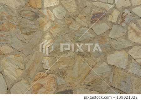 Textured stone wall with a natural color palette showcasing earthy tones and rustic charm in bright daylight Textured stone wall with a natural color palette showcasing earthy tones and rustic charm in bright daylight 139021322