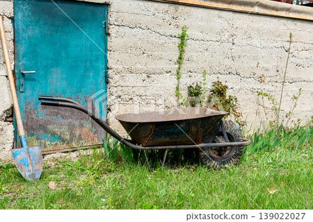wheelbarrow and garden tools in front of concrete wall wheelbarrow and garden tools in front of concrete wall 139022027