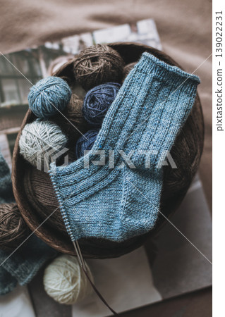 Hand knitted socks with needles and yarn ball in a basket. Concept for handmade and hygge slow life. Hand knitted socks with needles and yarn ball in a basket. Concept for handmade and hygge slow life. 139022231