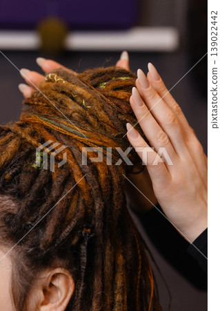 Hands braiding dreadlocks with decorative threads close up Hands braiding dreadlocks with decorative threads close up 139022442