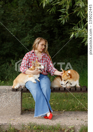 Woman With Dogs. Gentle Woman Enjoying Quiet Moment With Two Corgis In Lush Green Park Setting Woman With Dogs. Gentle Woman Enjoying Quiet Moment With Two Corgis In Lush Green Park Setting 139022445