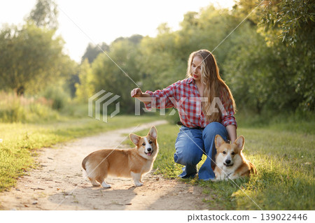 Young Woman And Corgi Playing. Caucasian Woman Kneels Down Outdoors With Her Corgi Puppy Young Woman And Corgi Playing. Caucasian Woman Kneels Down Outdoors With Her Corgi Puppy 139022446