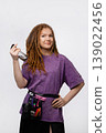 Smiling female braider with dreadlocks holding spray bottle isolated on white background 139022456