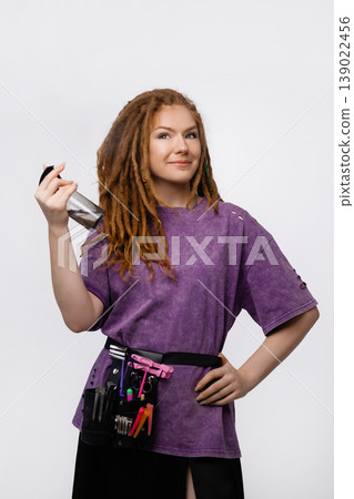 Smiling female braider with dreadlocks holding spray bottle isolated on white background Smiling female braider with dreadlocks holding spray bottle isolated on white background 139022456