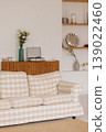 Beige plaid sofa standing in living room with white wall, wooden cabinet and flowers 139022460