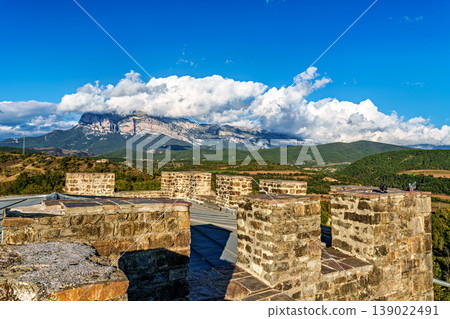 Ainsa Castle in the medieval village of Ainsa in Spain surrounded by stone walls with an elevated path leading to it. Ainsa Castle in the medieval village of Ainsa in Spain surrounded by stone walls with an elevated path leading to it. 139022491