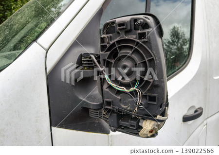 Broken side mirror on a white delivery van with exposed wiring and missing glass, parked outdoors after vehicle damage 139022566