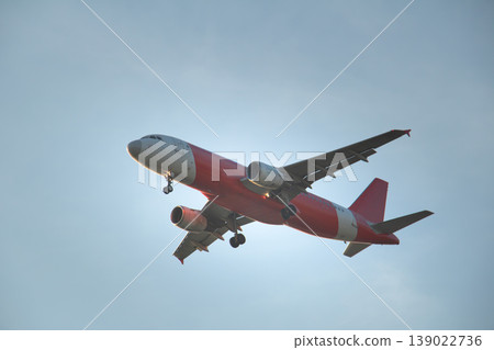 Low angle view of a red and white passenger airplane descending with deployed landing gear, captured against a clean blue sky, ideal for aviation, travel, and modern transport themes. Low angle view of a red and white passenger airplane descending with deployed landing gear, captured against a clean blue sky, ideal for aviation, travel, and modern transport themes. 139022736